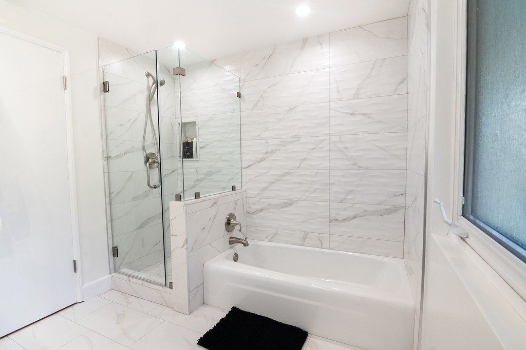 A bathroom with a glass-walled shower and a separate bathtub in white marble-look tile