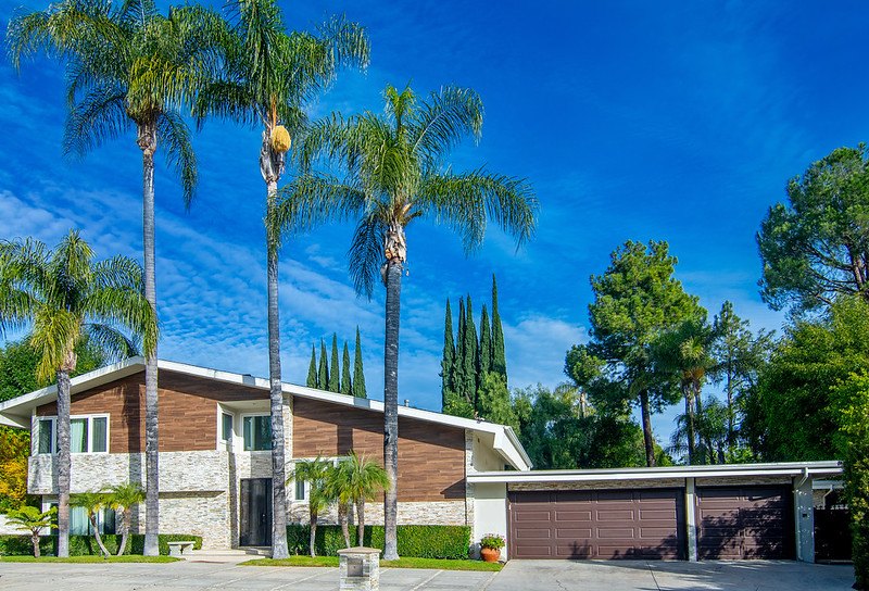 The front of the Winnetka home with its stone and wood facade, tall palms and a two-car garage